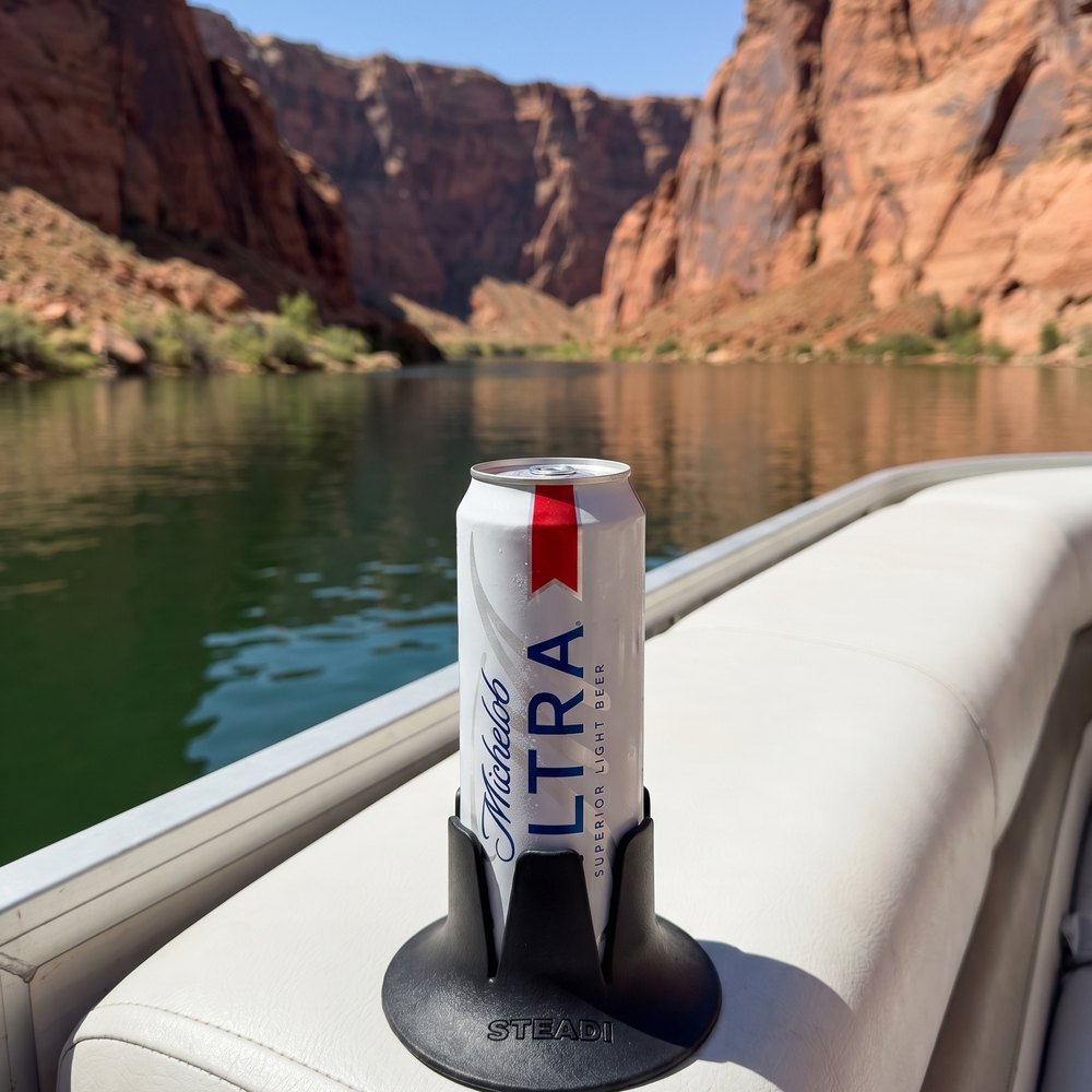 A can standing in a black Steadi on a white bench cushion beside open water.
